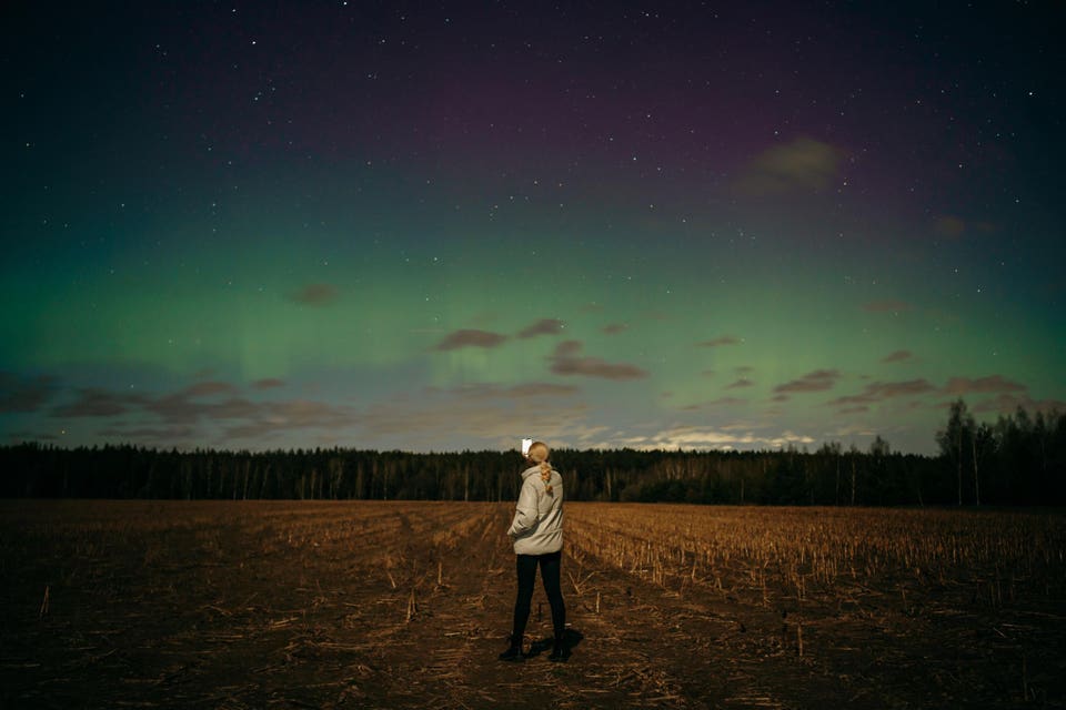 woman takes a photo of Aurora on a smartphone in field