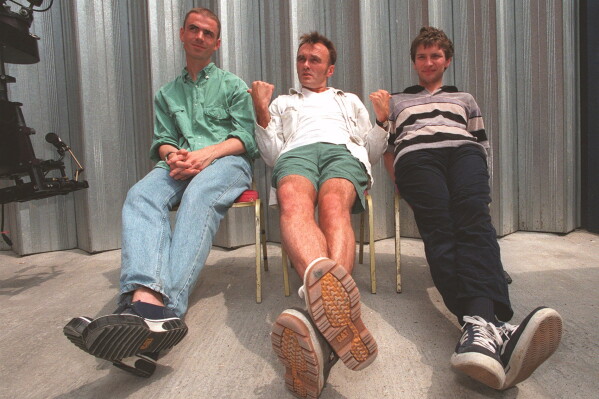 John Hodge, screenwriter for "Trainspotting," left, director Danny Boyle, center, and producer Andrew Macdonald appear during a music video shoot in London on June 26, 1996. (AP Photo/Louisa Buller, File)