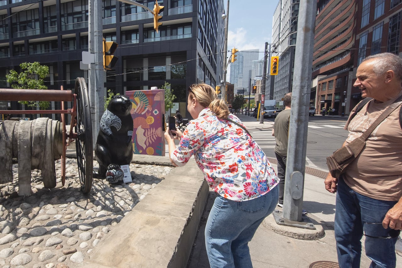 2 tourists take a photo of a beaver statue in downtown Toronto on a sunny spring day