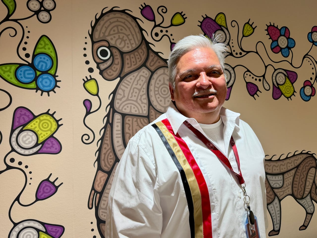 A man smiles at the camera in front of a patterned wall