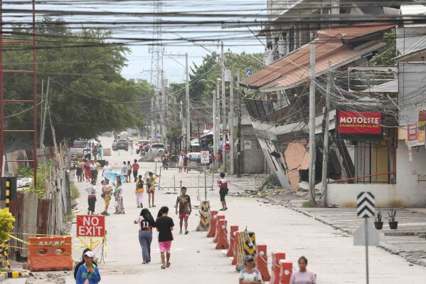 People walk past a collapsed building following an earthquake in Sarangani province, Philippines Wednesday, June 10, 2026. (AP Photo/Basilio Sepe)