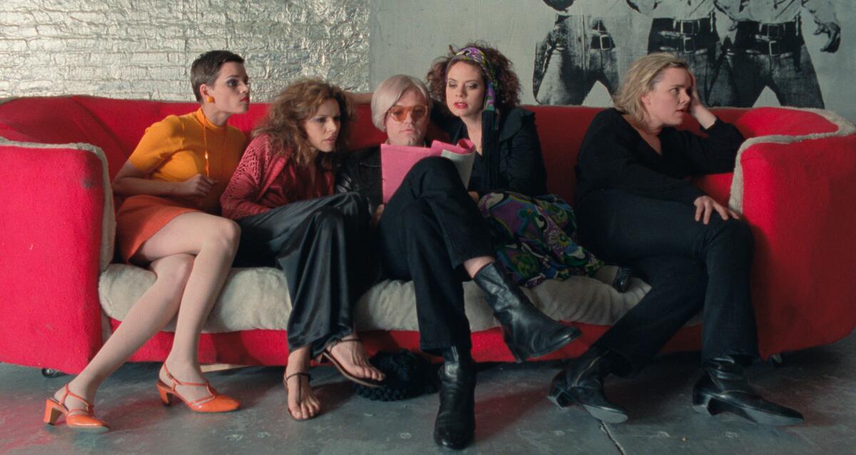 Several women share a couch with a man in a wig.
