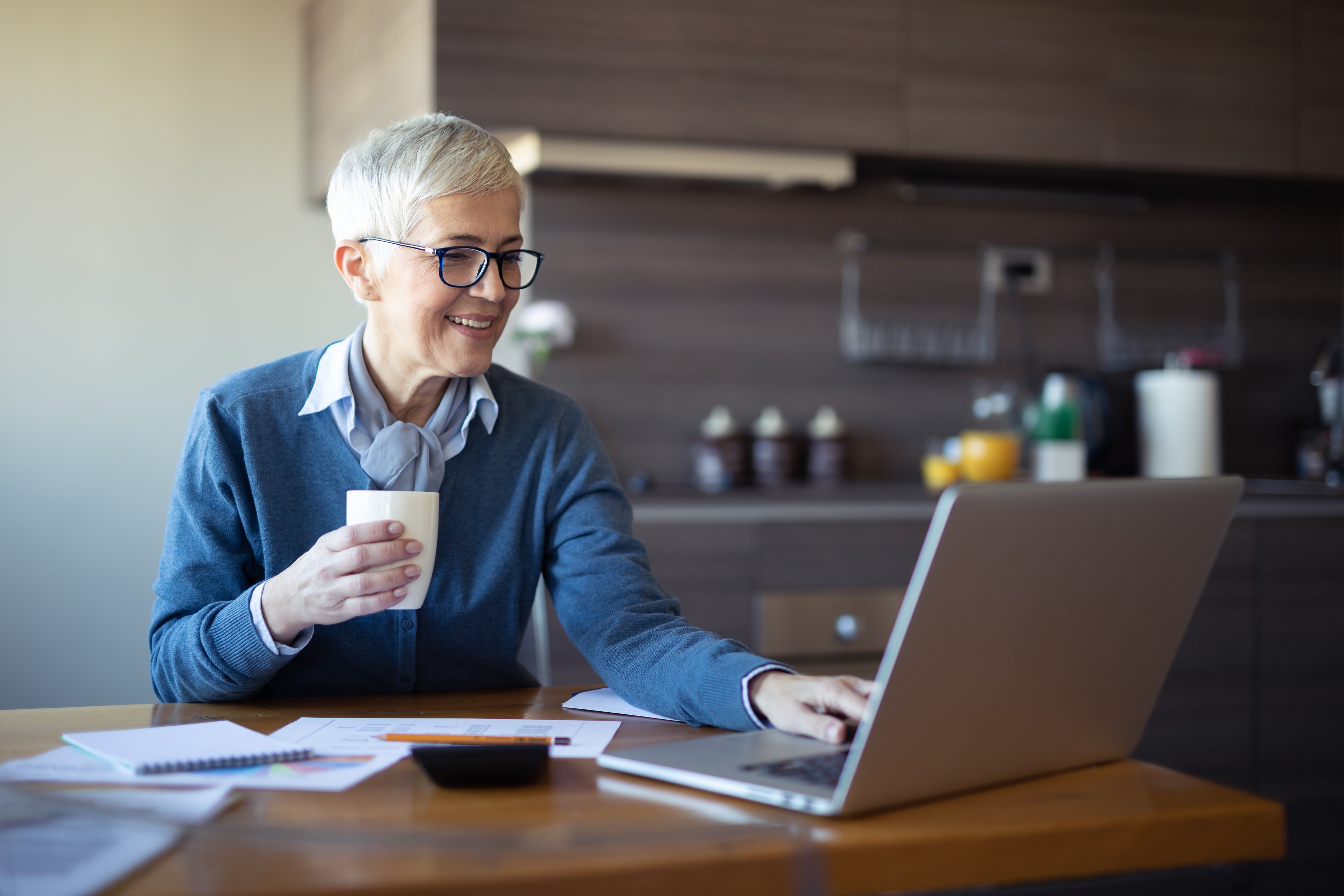 A retiree seated at a table is using a laptop.