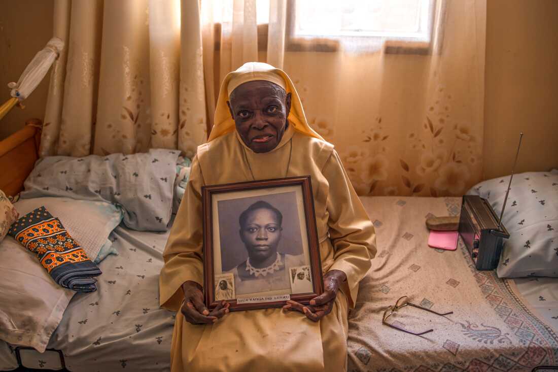 An elderly nun sits on her bed holding a portrait of her late mother at the Little Sisters of St Francis premises in Nkokonjeru, Uganda on May 12, 2026. The photograph is kept among her personal belongings inside the room where she lives within the congregation’s residential compound. The Little Sisters of St Francis, a longstanding religious congregation in Uganda, provide ongoing care and support for aging and retired sisters who continue to live within the convent after decades of service in education, healthcare, and community outreach. Many elderly sisters now rely on assisted care as they navigate old age within the religious community they have spent their lives serving.