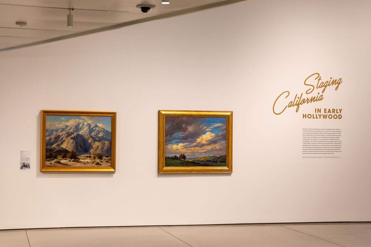 Two paintings, one of mountains and one of a field below a graying sky, hang on a white wall.