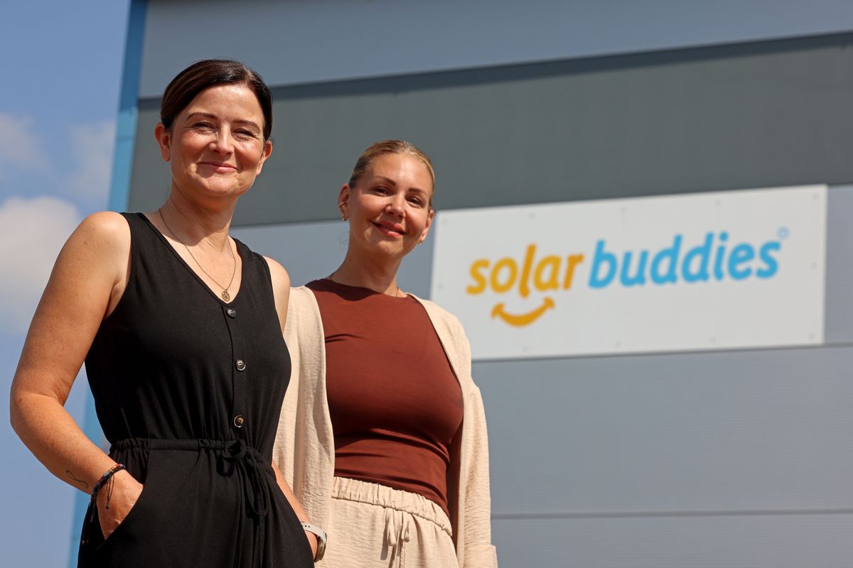 Two smiling women stood together outside in front of a building with branding for a business