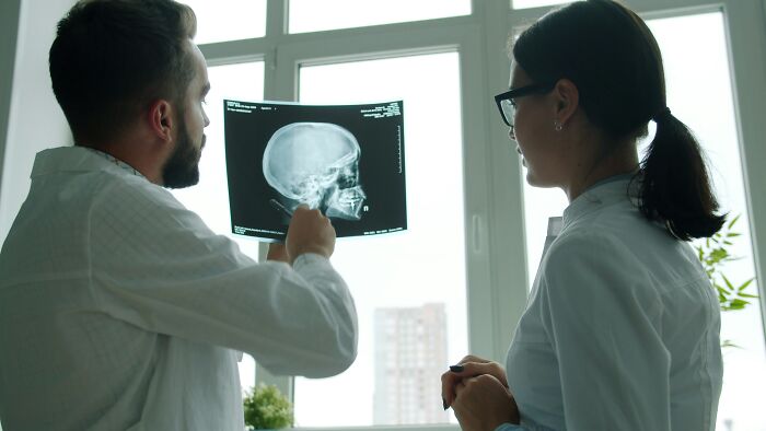 Two nurses examine a skull X-ray, discussing a patient's medical condition and potential diagnoses.