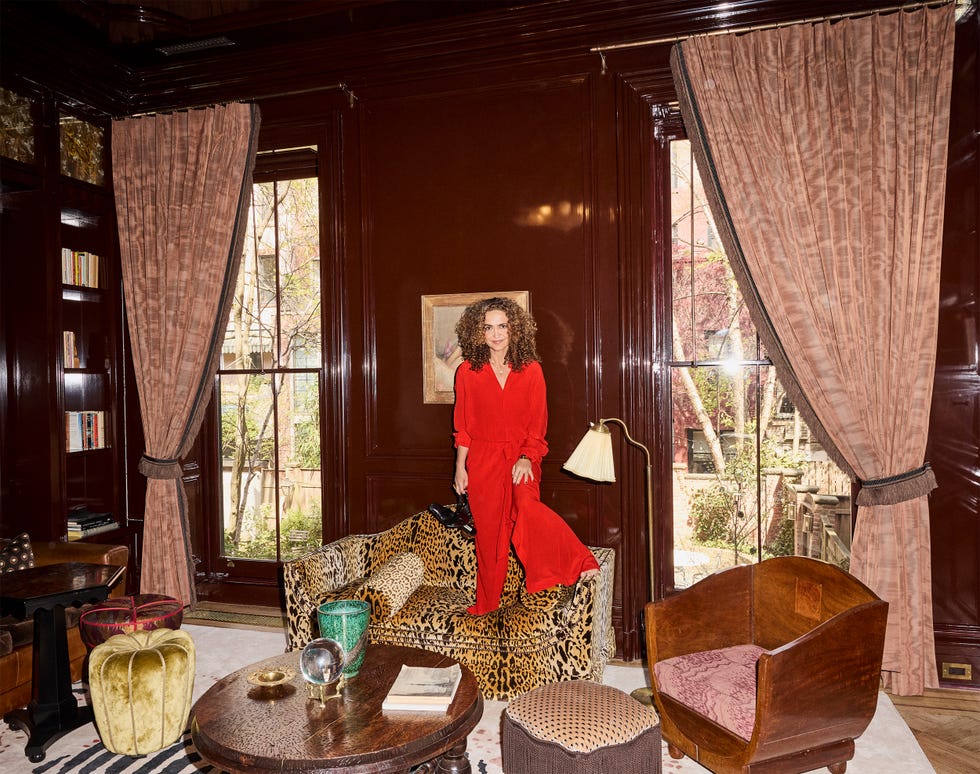 Person in red outfit standing on leopard print couch in elegant room with large windows and brown decor.