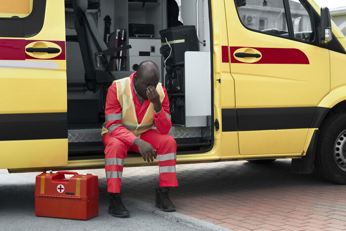 Distressed paramedic sitting by an ambulance, pondering unexplained events with patients.