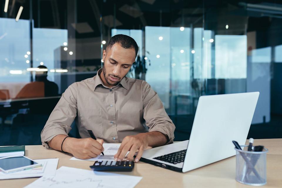 A middle-aged person is sitting at a desk while using a calculator. 