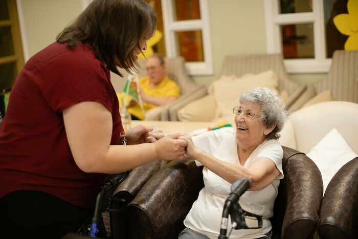 A nurse holding hands with an elderly patient, both smiling. The nurse provides care to patients.