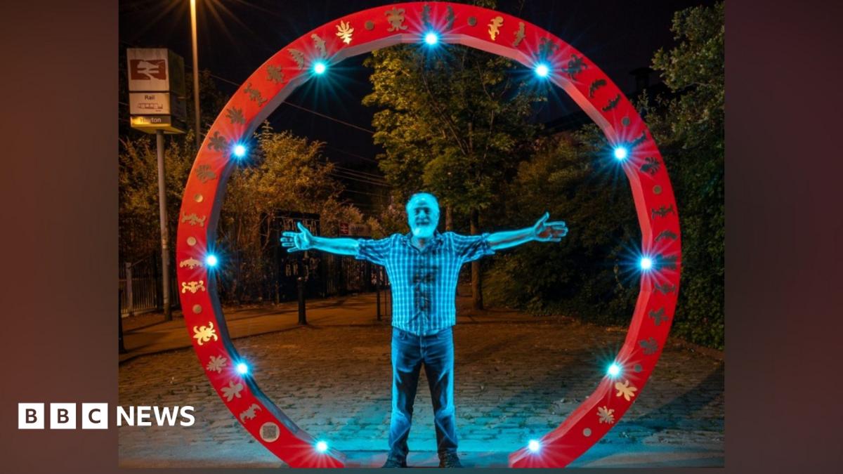 Man stands inside red circle sculpture with hands out - Martin Heron in the Family Circle, part of the Art Around Huyton project