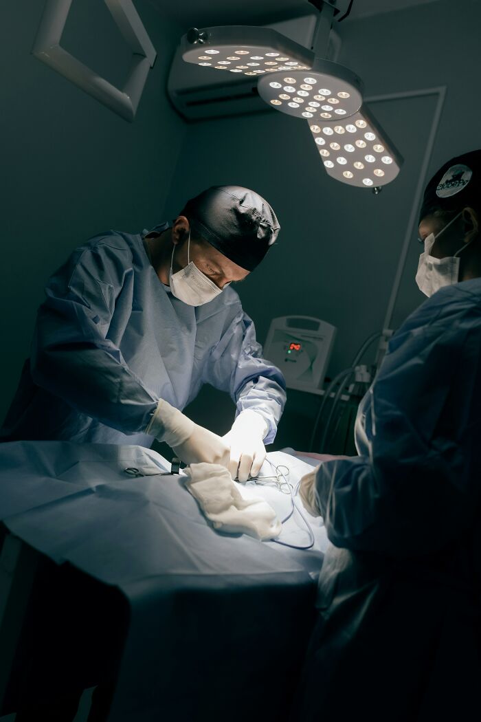Two nurses perform surgery under bright operating room lights, focusing on the patient's intricate procedure.
