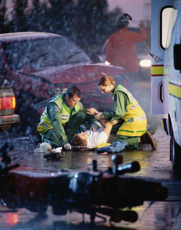 Nurses attend to a patient on a stretcher at a car accident scene, providing emergency medical assistance.