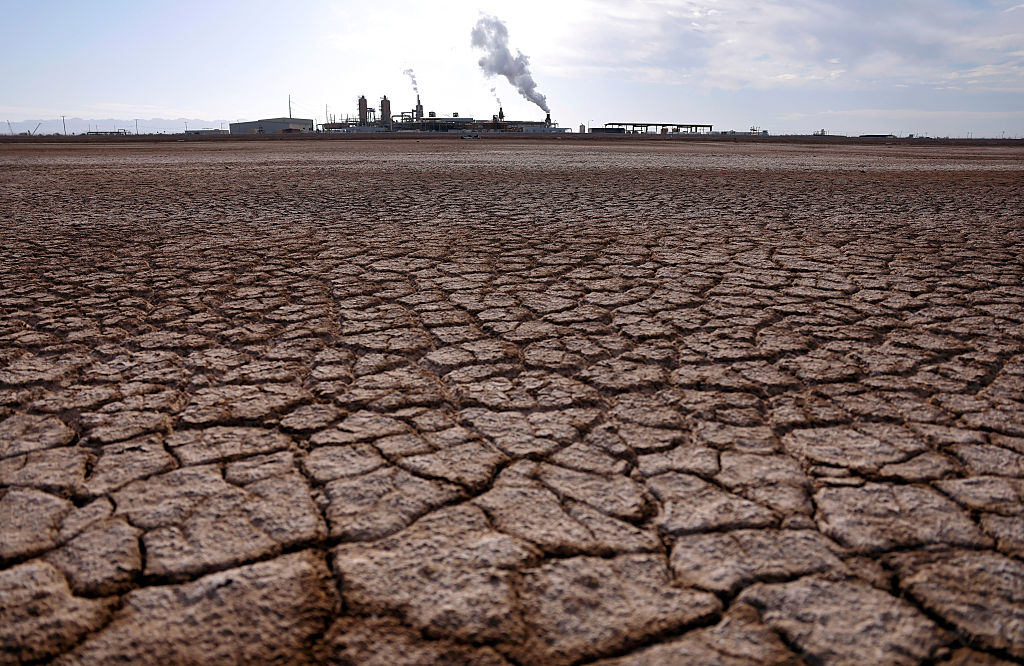 Dry, cracked soil at the Salton Sea in California. We see a geothermal power plant in the background.