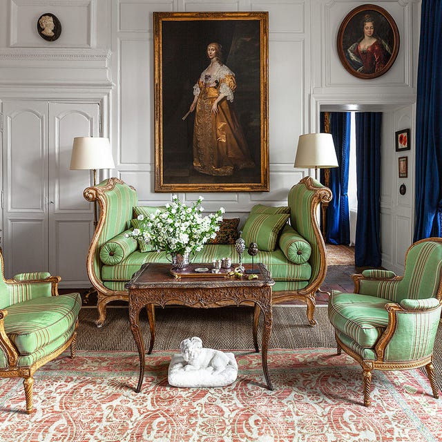 Elegant sitting room with green striped chairs, ornate table, classical paintings, and deep blue curtains.