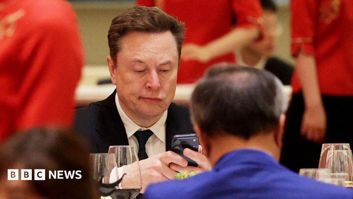 A man in a suit and tie stares at his phone while sitting down opposite a man in a blue jacket in Beijing