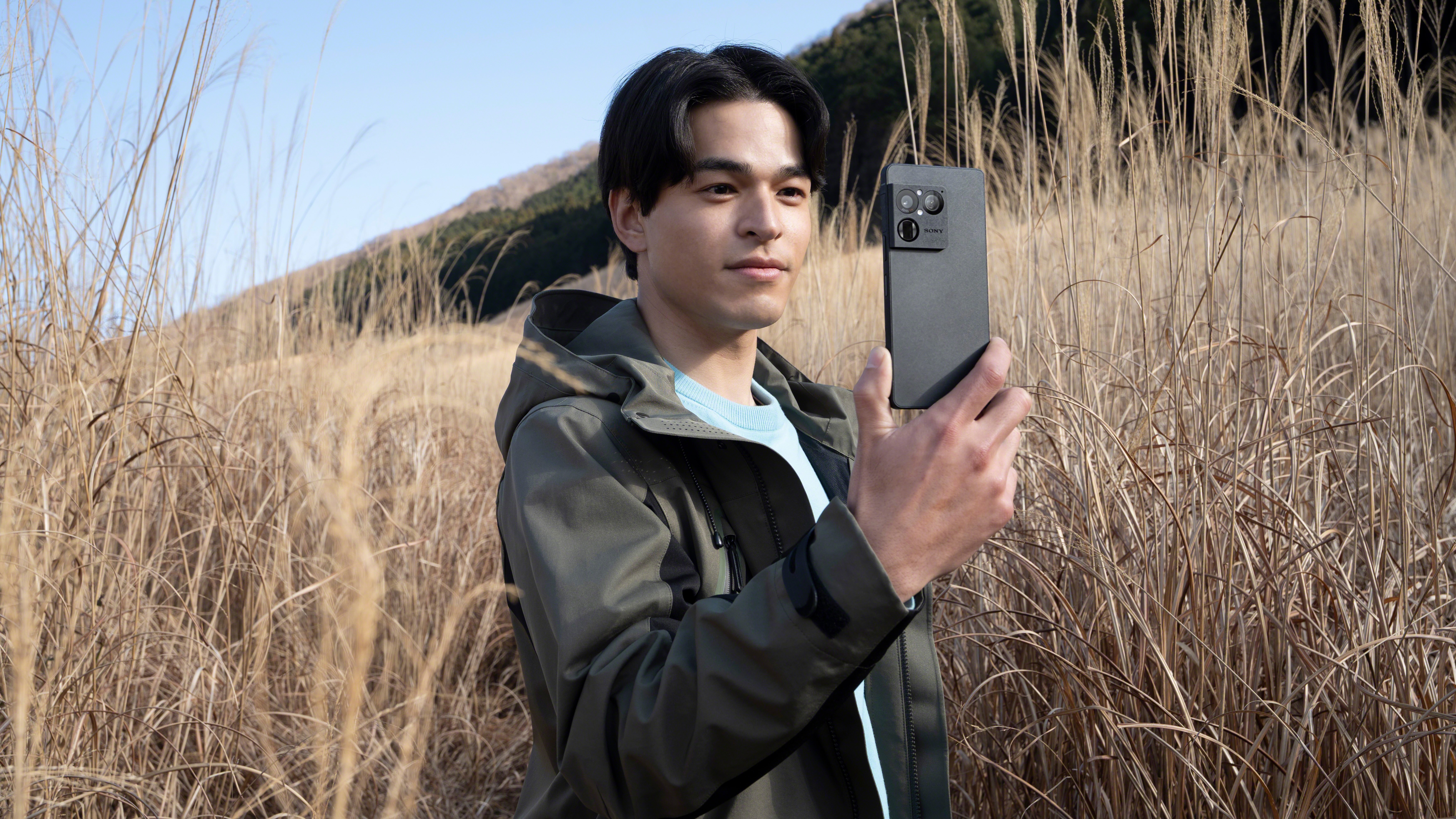 Sony Xperia 1 VIII phone held up by a person in a field of tall grass