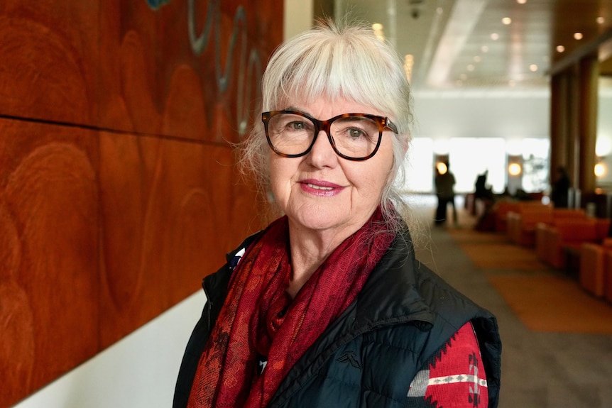 A woman wearing glasses standing next to artwork smiling at the camera