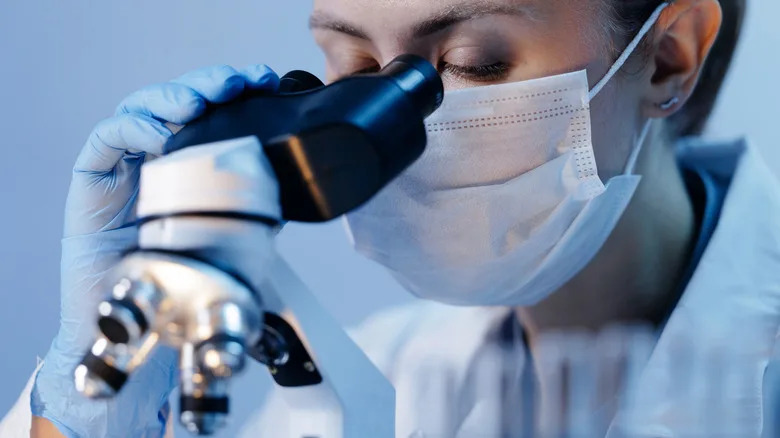 Person wearing a face mask looking into a microscope