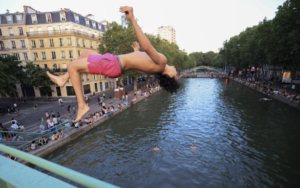 A youth jump from a bridge into the Canal Saint-Martin as France experiences a heatwave, in Paris on June 25, 2026. Due to the ongoing heatwave sweeping across France - the Bassin des Recollets - a portion of the Canal Saint-Martin in the French capital has been opened for swimming from June 17. (Photo by Ludovic MARIN / AFP)