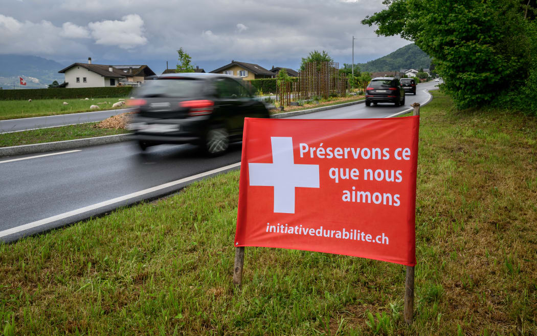 This photograph shows an election banner adorned with a Swiss cross reading in French "Let’s preserve what we love" beside a road ahead of the vote on the "No to 10 Million" immigration initiative, in Muraz on May 10, 2026. The "No to 10 million" immigration initiative proposed by the right-wing Swiss People's Party, which aims to limit Switzerland’s permanent resident population to 10 million by 2050, will be put to a nationwide vote on June 14, 2026. (Photo by Fabrice COFFRINI / AFP)