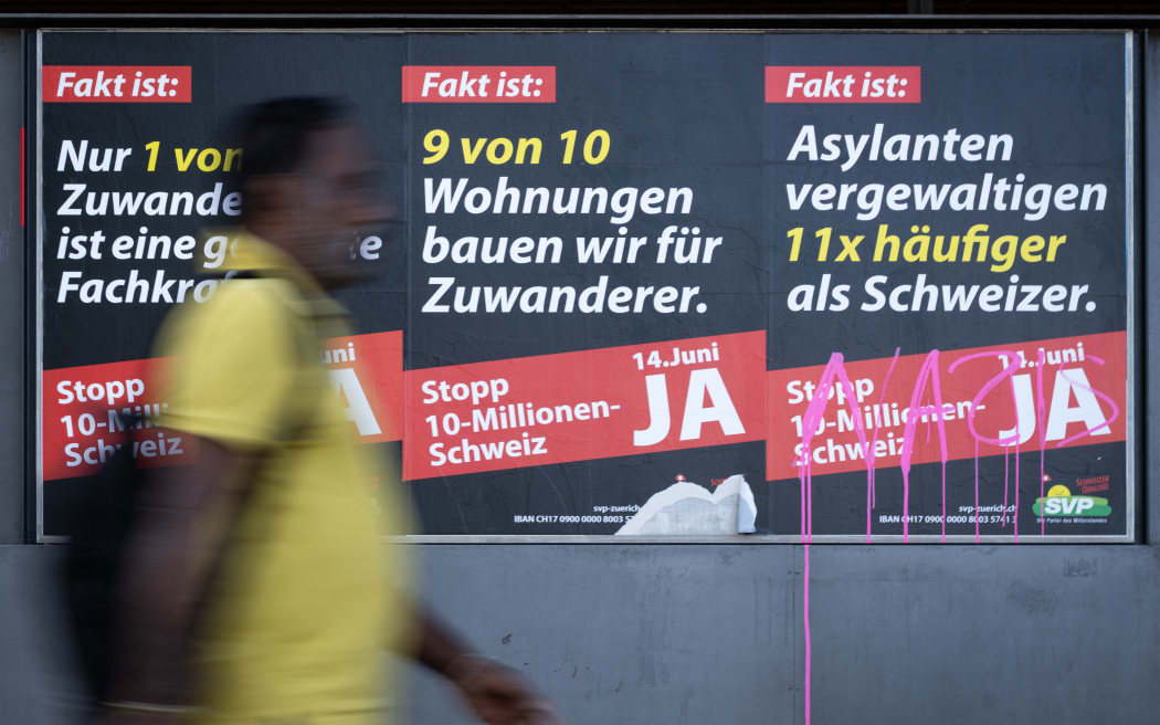 A man passes by posters campaigning for the "yes" vote at next June 14's initiative launched by the hard-right Swiss People's Party (SVP) to cap the population at 10 million, an anti-immigration proposal that is fracturing public opinion in the wealthy Alpine nation, in Zurich on May 28, 2026. The panels slogans read in German (from L) : "The fact is: Only 1 in 10 immigrants is a skilled worker in demand", "The fact is: We build 9 out of 10 homes for immigrants" and "The fact is: Asylum seekers commit rape 11 times more often than Swiss nationals" (Photo by SEBASTIEN BOZON / AFP)