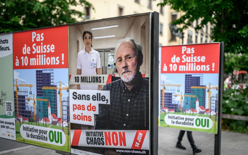 This photograph shows campaign posters for and against a nationwide vote on an anti-immigration initiative, reading (L and R) "No to a Switzerland of 10 million!" and (C) "Without her, there would be no care," in Geneva on June 4, 2026. The Swiss will vote on June 14, 2026, on an initiative to cap the population at 10 million -- an anti-immigration proposal that is fracturing public opinion in the wealthy Alpine nation. "No to a Switzerland of 10 million inhabitants," is the name of the project launched by the country's biggest party, the hard-right Swiss People's Party (SVP), renowned for its opposition to immigration and closer ties with the European Union. (Photo by Fabrice COFFRINI / AFP)