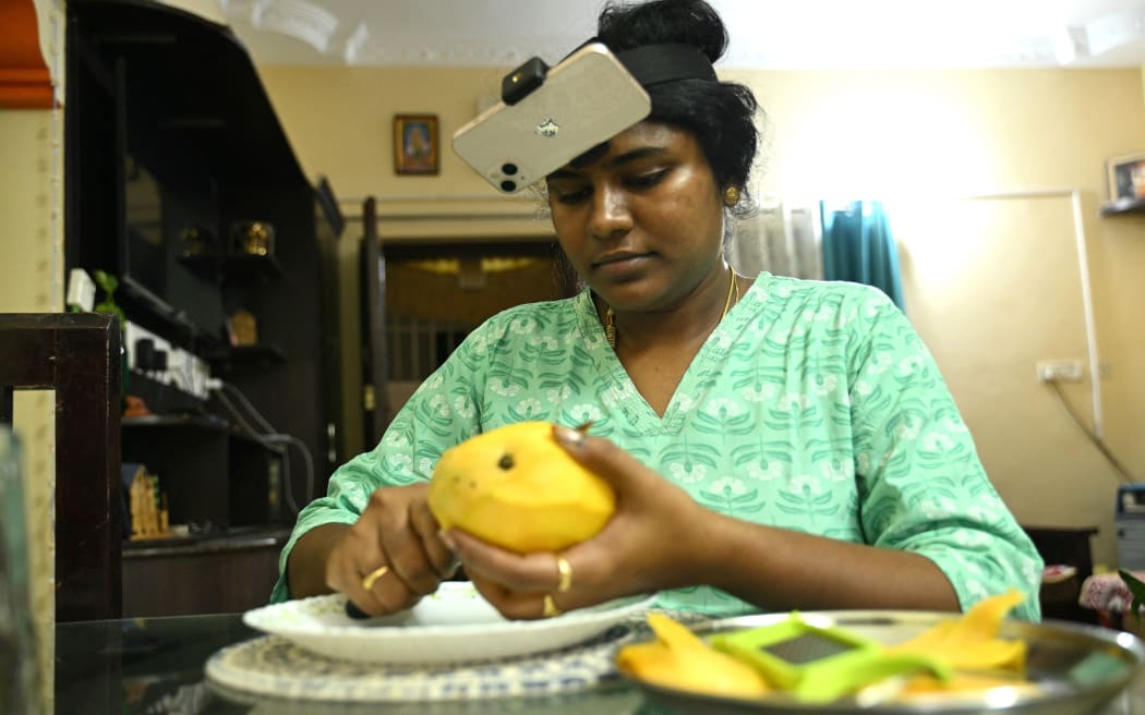 This photograph taken on May 15, 2026 shows an Indian housewife Nagireddy Sriramyachandra wearing a smartphone on her head as she records her actions through motion capture while slicing mangoes at her home in Chennai. Developers think feeding first-person footage, called
