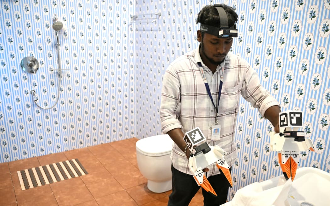 This photograph taken on May 13, 2026 shows a worker wearing a GoPro camera on his head recording actions through motion capture while folding towels inside a model bathroom at AI data company Objectways' office in Tamil Nadu's Karur district. Developers think feeding first-person footage, called "egocentric data", into specialised AI models will help robots copy humans. The humanoid robot market is booming, with investment bank Morgan Stanley predicting there could be over a billion in use by 2050, mostly for industrial and commercial purposes. In India, the emerging field of spatial AI is providing new employment -- for now. (Photo by R.Satish BABU / AFP)