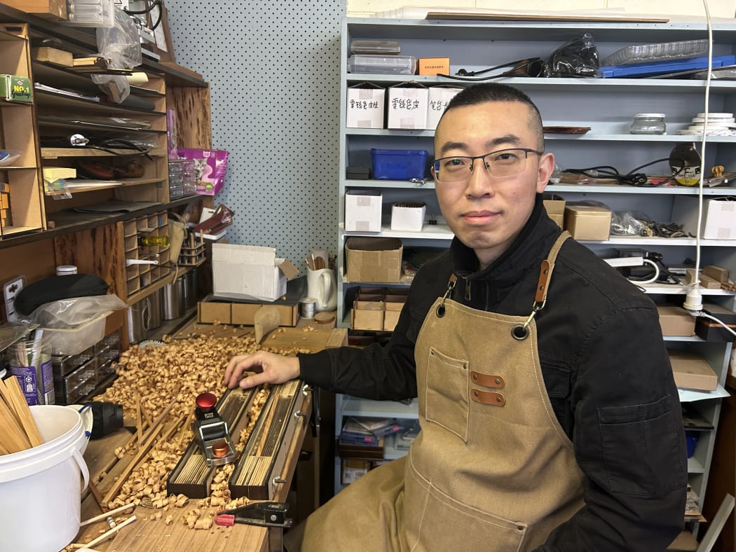Picture shows a man smiling at the camera, with woodworking tools in the background