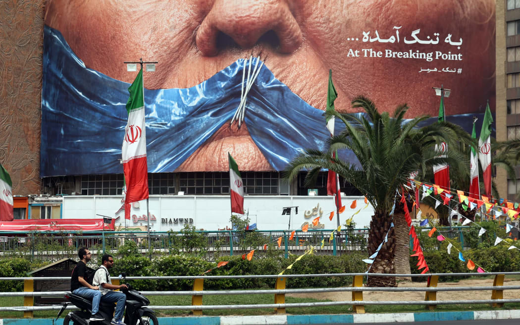 Iranians drive past a billboard featuring US President Donald Trump and the Strait of Hormuz, erected on Valiasr Square in Tehran May 28, 2026. Iran's foreign ministry condemned on May 28, what it called violations by the United States after its strikes on the southern port city of Bandar Abbas and expressed solidarity with Oman after the US president threatened to "blow them up". (Photo by AFP) /