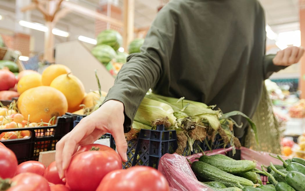 A woman reaches to grab a tomato from the grocery section in a supermarket.