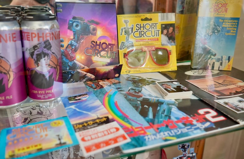 cabinet with various DVDs, magazines and a pair of glasses all branded for the movie Short Circuit