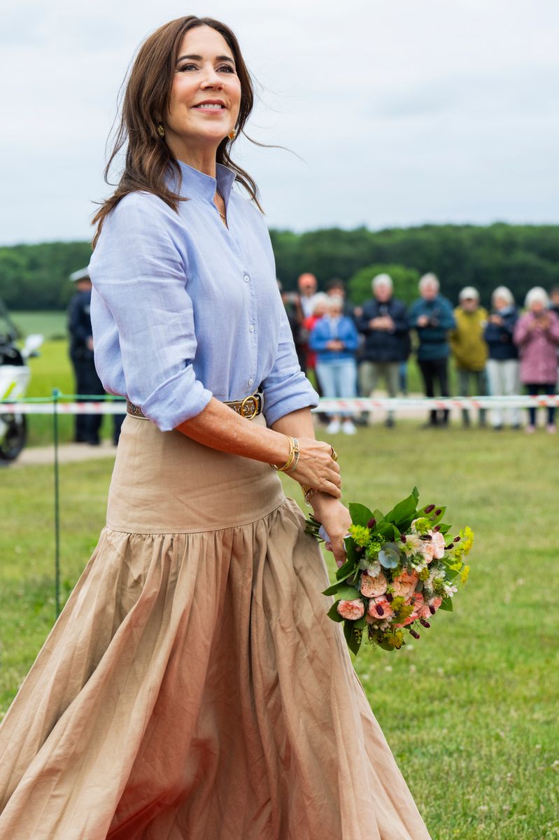 Queen Mary embraced understated elegance in a belted beige skirt, classic trench coat, and timeless cap-toe ballet flats during her latest royal engagement.