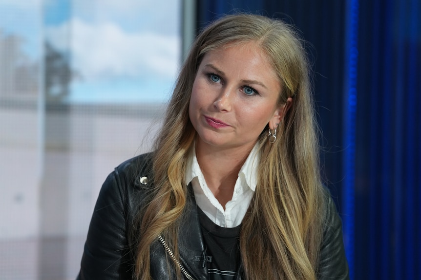 Grace, a young woman with blonde hair, sits in a TV studio.