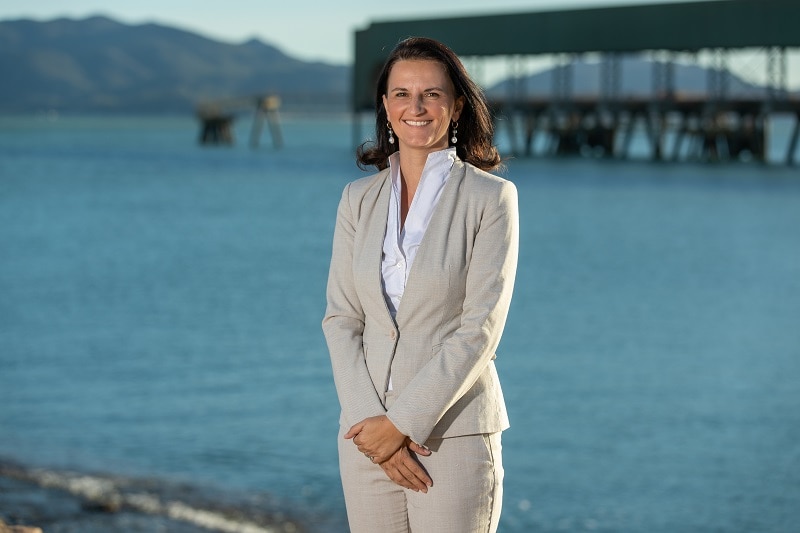 A woman smiling at the camera, with a blue sea and port infrastructure in the background