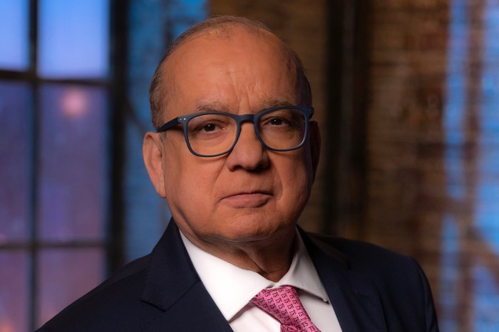 Touker Suleyman. for Dragon's Den, wearing a blue suit, white shirt and pink tie.