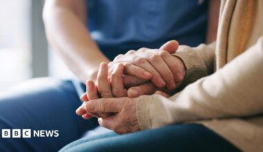 A stock photo of a close up of two people holding hands in a supportive way.