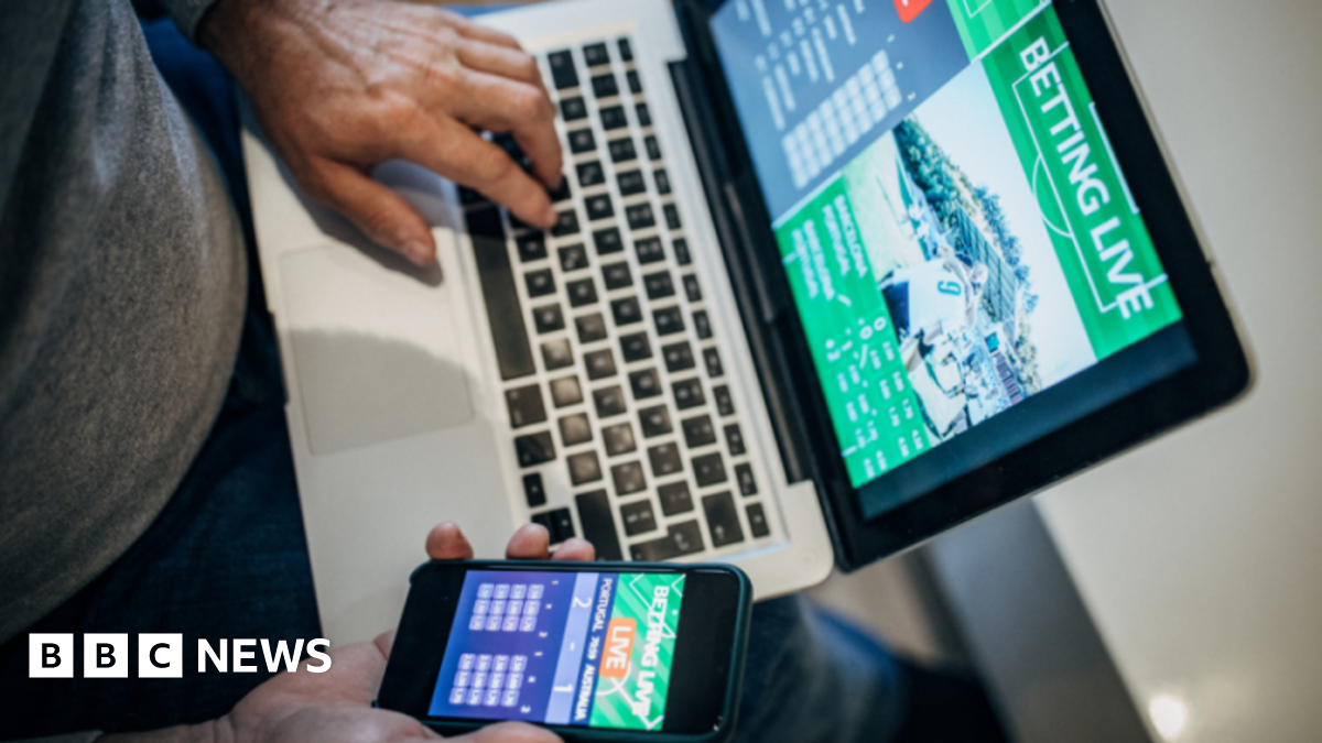 Man accessing gambling platforms online via laptop and phone app.