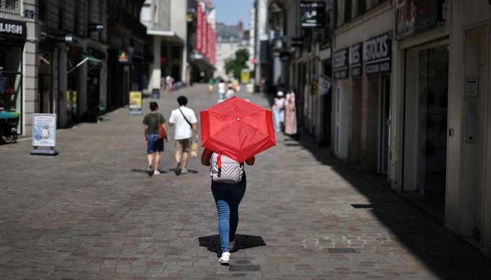 A woman uses a red umbrella to shade from the sun while walking on a street in Nantes as temperatures rise during a heatwave affecting a large part of France, June 22, 2026.