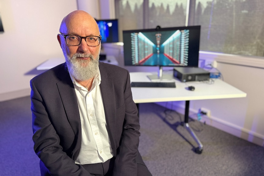 Russell Kelly sitting in front of computers in an office.