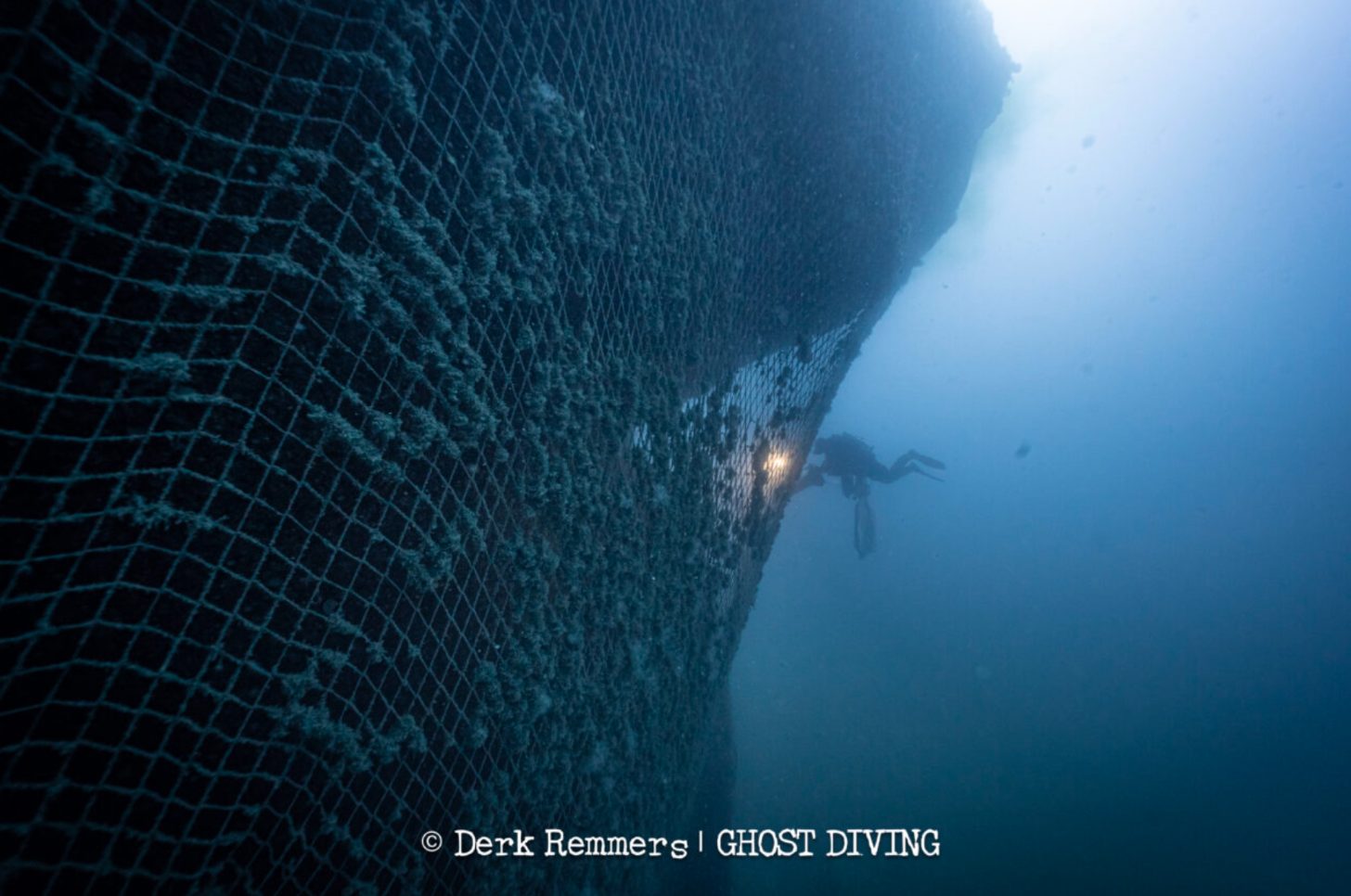 A diver is seen investigated massive netting attached to a shipwreck underwater