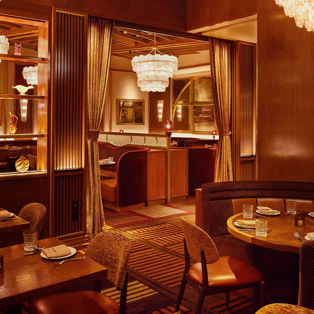 Elegant restaurant interior with soft lighting, patterned carpet, wooden furniture, and chandeliers.