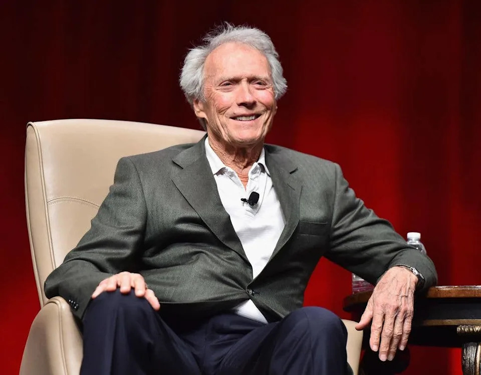 clint eastwood sitting in chair smiling at cinemacon 2015