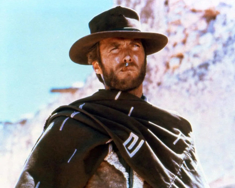 Clint Eastwood smoking a cigar, wearing a brown hat and poncho in a publicity portrait for the film, A Fistful of Dollars