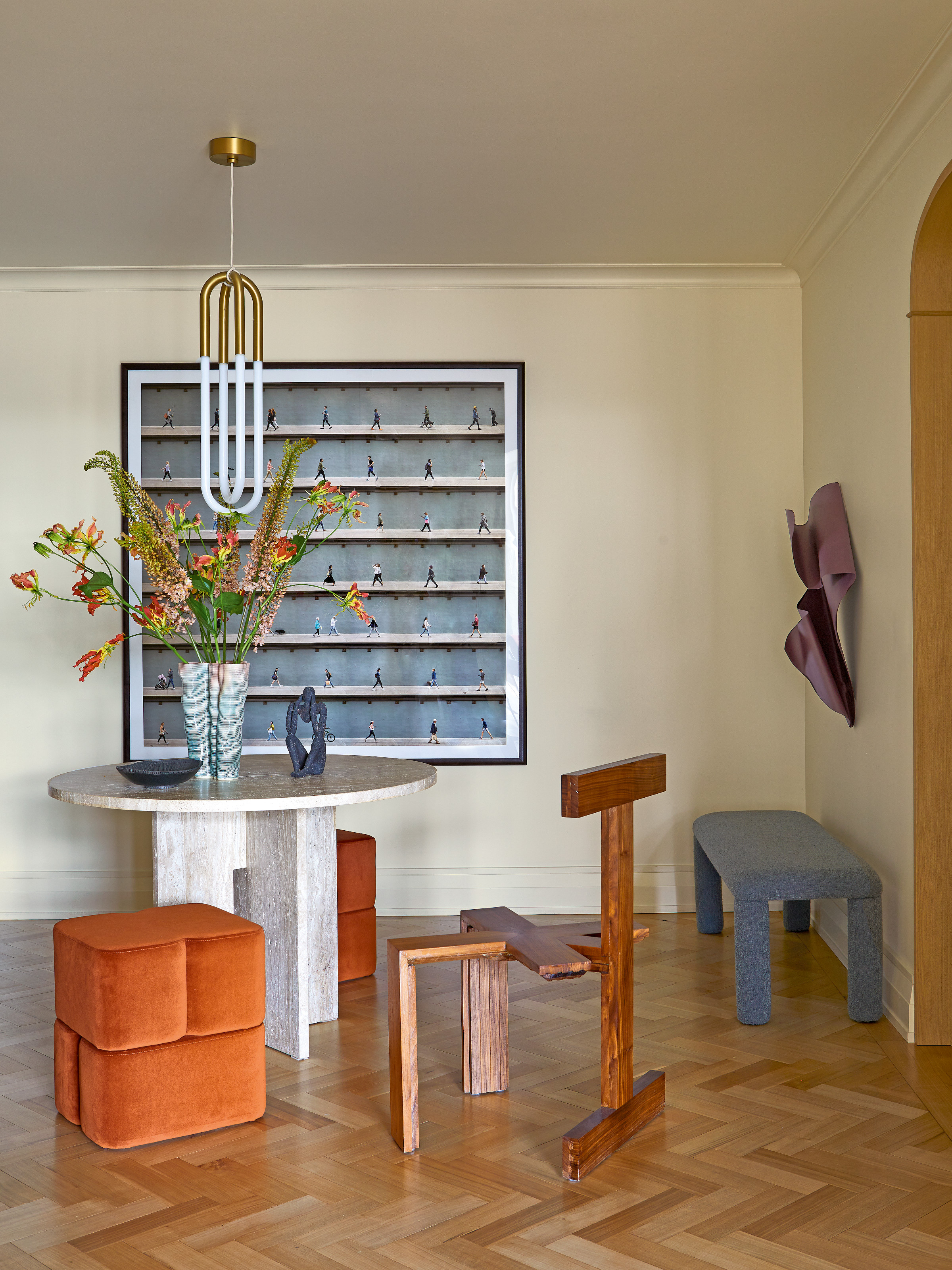 Dining area with white marble table, orange stools, blue bench, sculptural wood chair, square artwork and purple wall sculpture