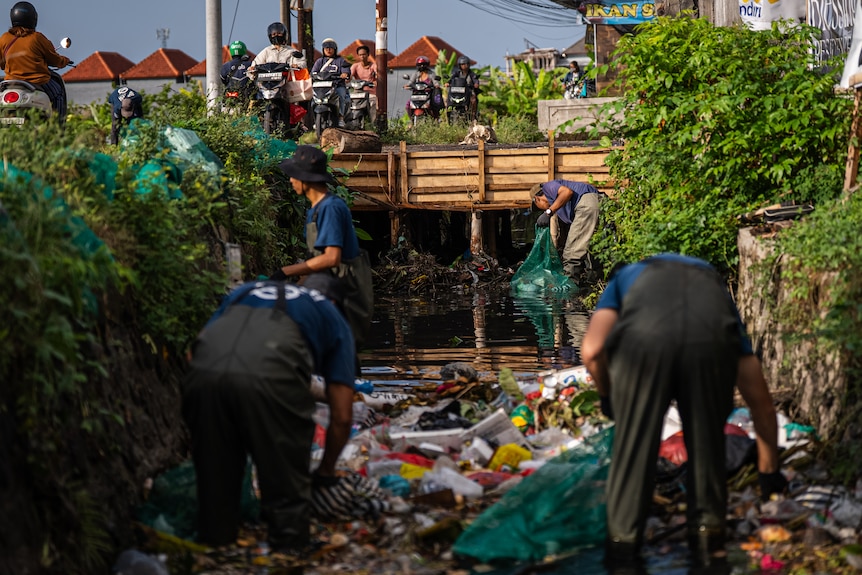 A group of volunteers clean up a river filled with trash in Bali.