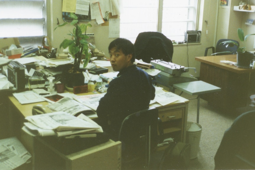 a sepia toned film photo of a man at a busy desk