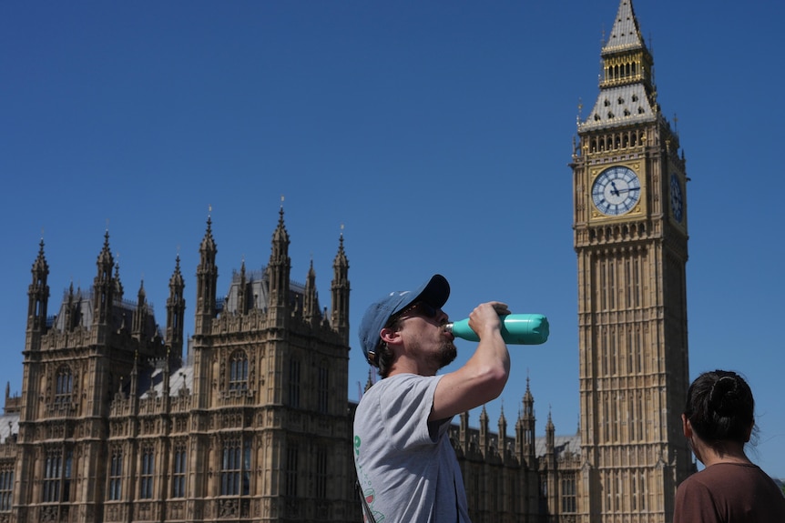 A man drinking from a water bottle out the front of Big Ben.